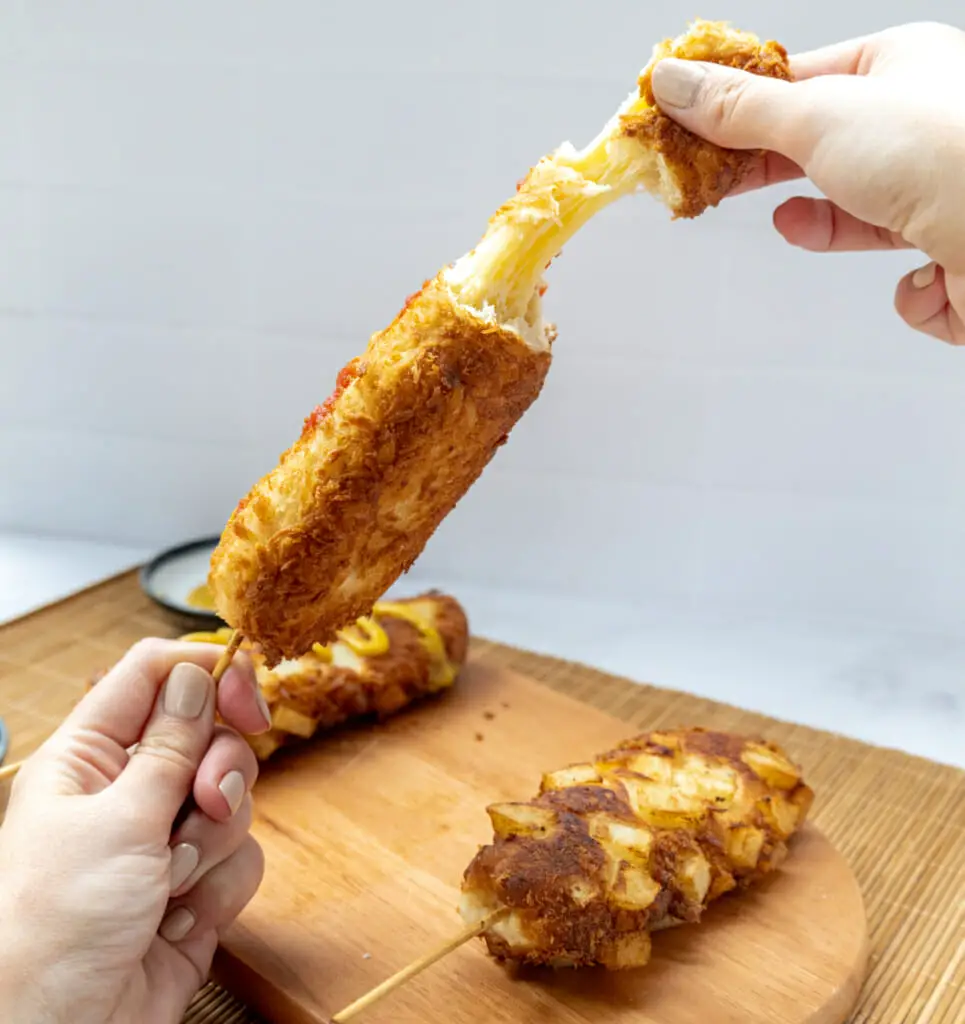 hand taking apart a korean corn dog with cheese on the inside