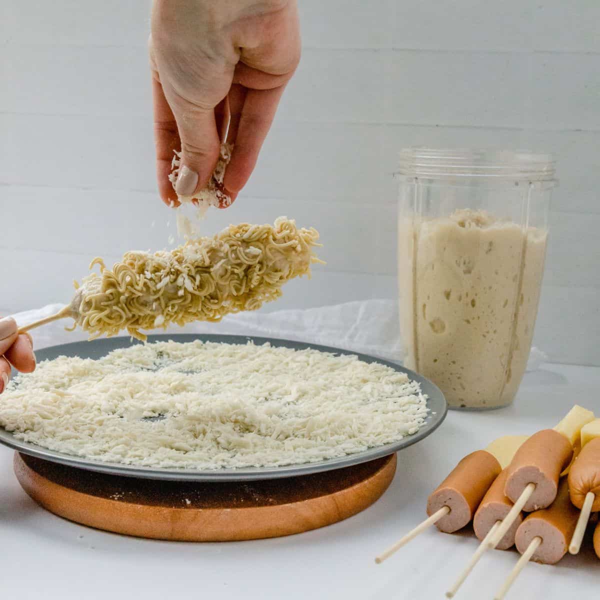 hand sprinkling crushed ramen noodle onto battered korean corn dog