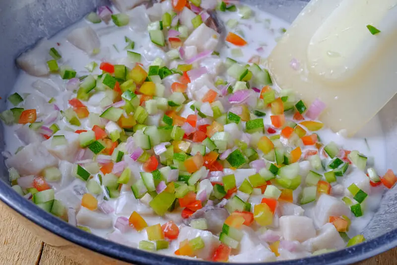 Adding chopped vegetables into fish and milk mixture and tossing