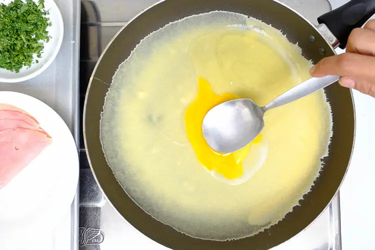 Adding an egg on top and spreading it evenly over crepe with a spoon