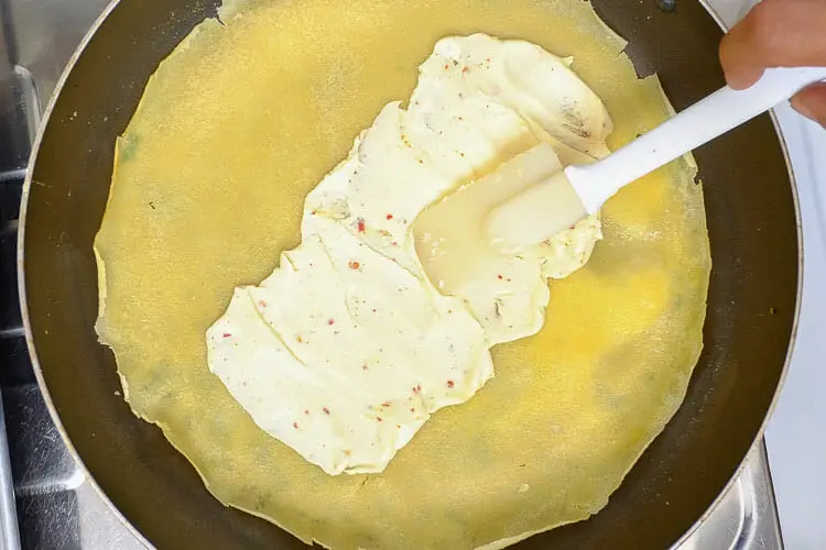 Spreading cream cheese on the middle of the crepe