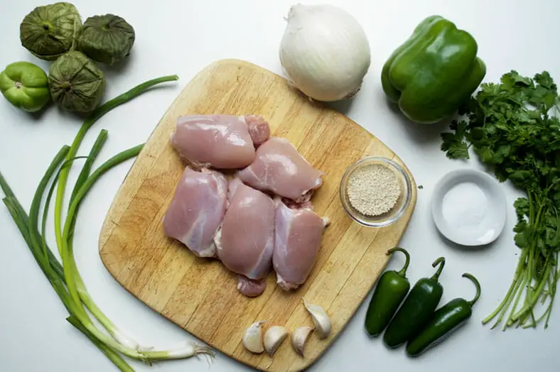 View of ingredients - chicken, chili pepper, onion, green bell pepper, jalapeno, tomatillos, sesame seeds, green onions