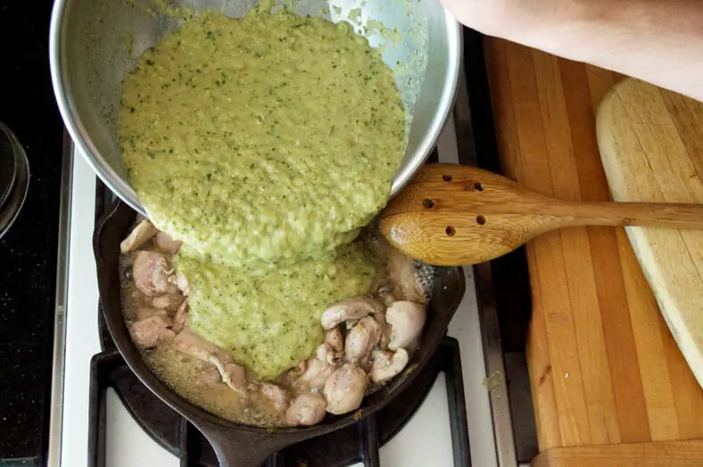 Adding vegetable green broth paste to chicken with wooden spoon