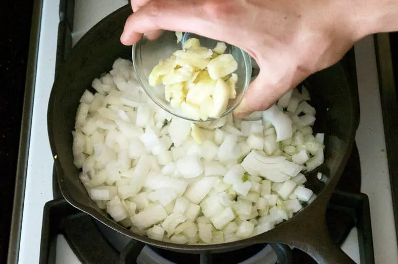Adding garlic to the cooked onions in pan