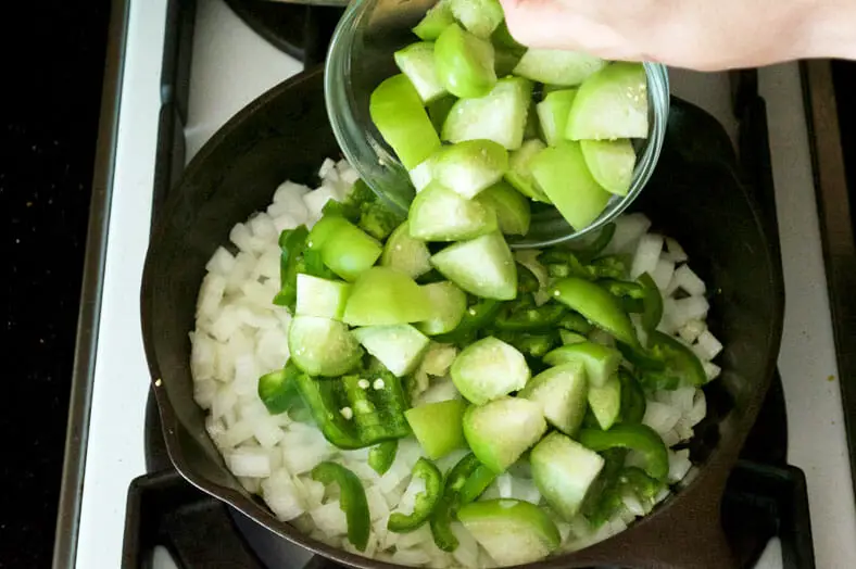 Adding tomatillos to the cooked onions in pan
