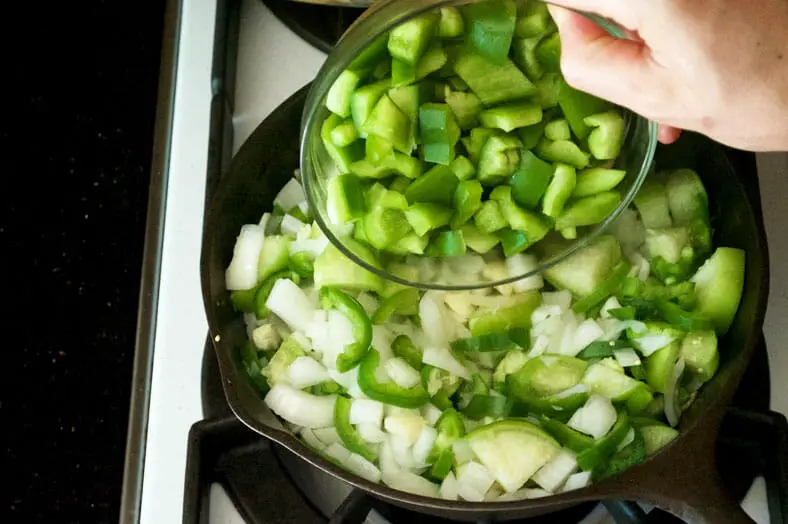 Adding green bell pepper to the cooked onions in pan