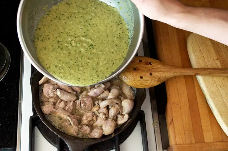 Adding green sauce to the cooking chicken in stockpot