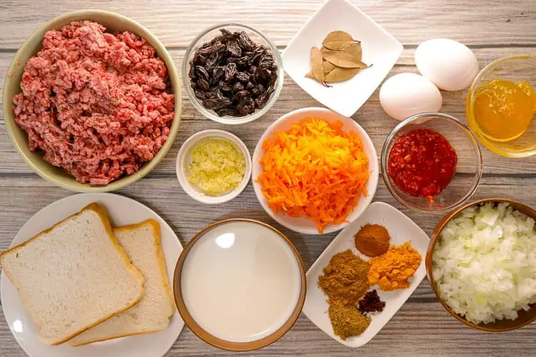 View of ingredients - lamb, beef, carrots, onions, garlic, raisins, spices, apricot jam, hot chutney, white bread soaked in milk, eggs