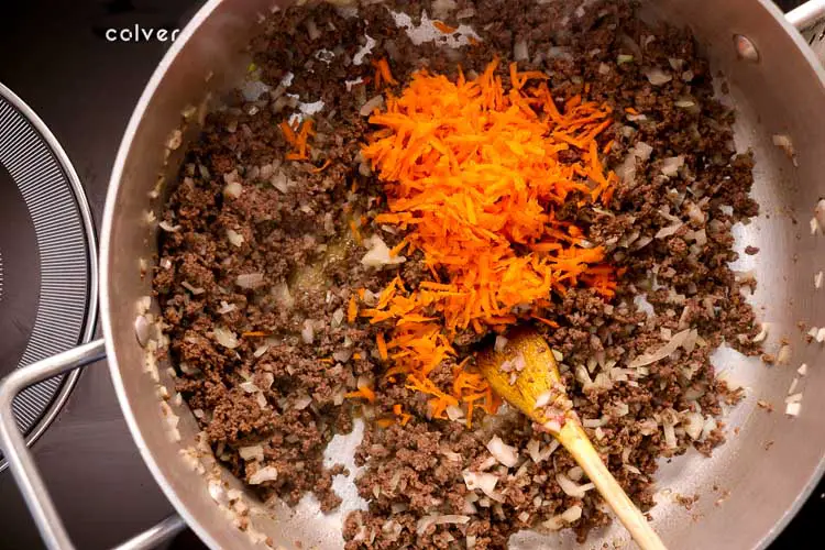 Adding grated carrots to the onion and mince mixture