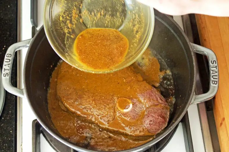 Adding spices micture to lamb in pot for cooking