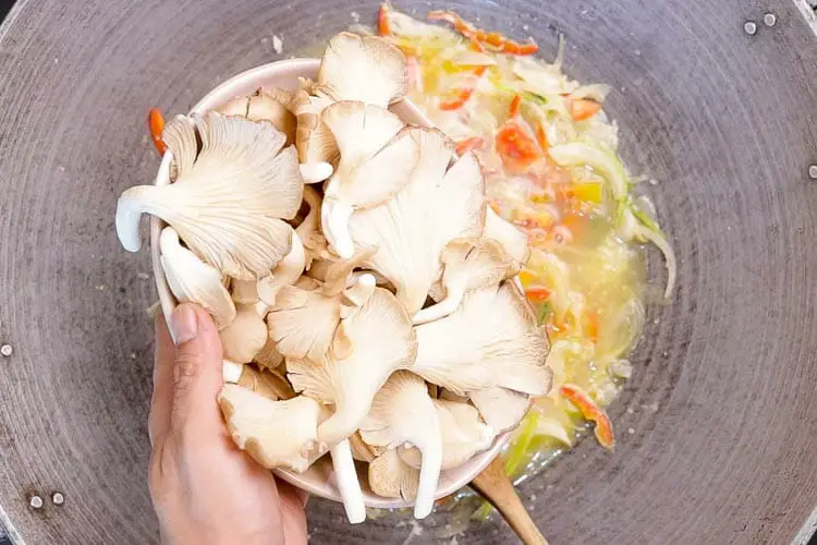 Adding oyster mushrooms in the wok to the mixture