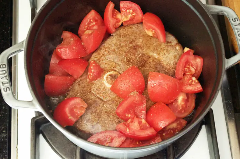 Adding big chunks of tomatoes to the lamb in pot