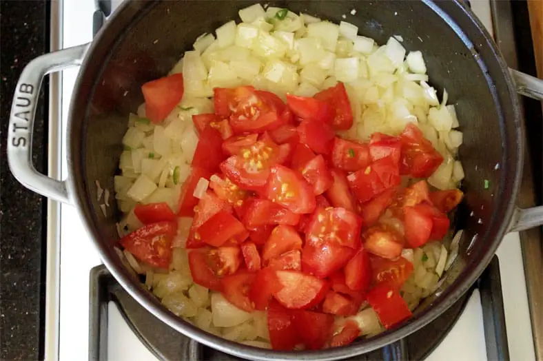 Adding tomato to onions in pot for cooking