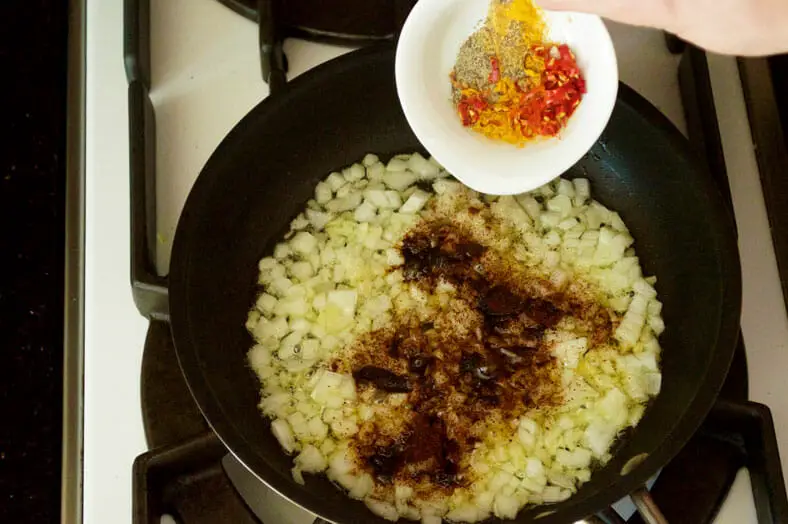 Adding onion and spices to the pan for cooking