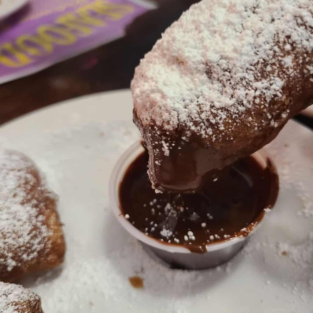 Dusted fluffy French treat with powdered sugar dipped in chocolate sauce