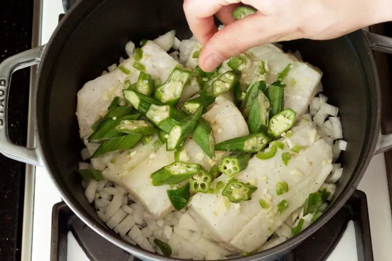 Adding sliced okra to pot with fish and vegetables