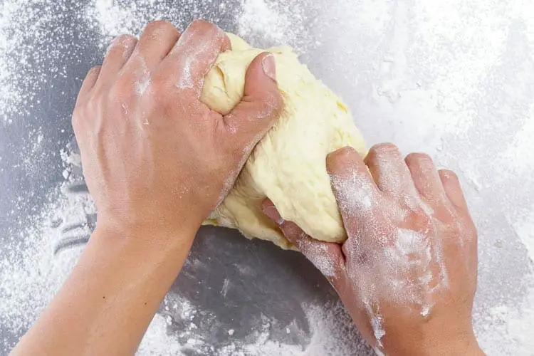 top view of hands kneading, rolling, and pulling on dough