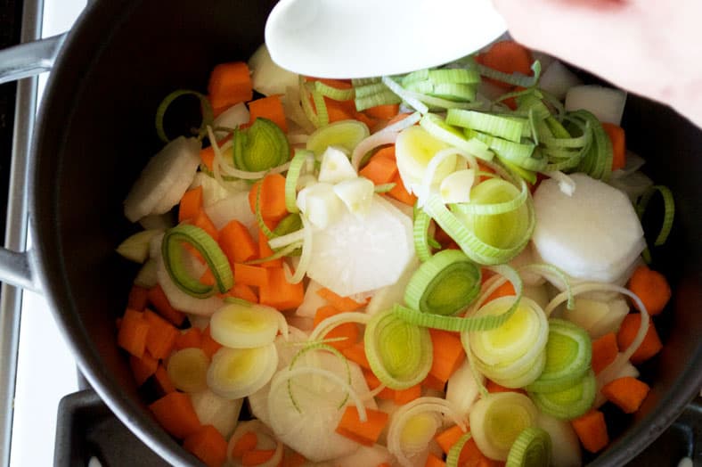 Adding carrots, onions, radish in stockpot for cooking