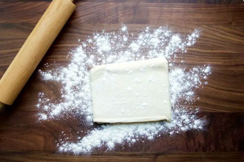 Puff pastry dough sprinkled with flour on wooden surface