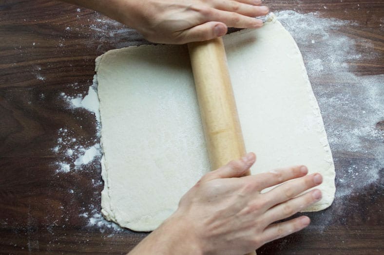 Rolling dough on wooden surface with rolling pin
