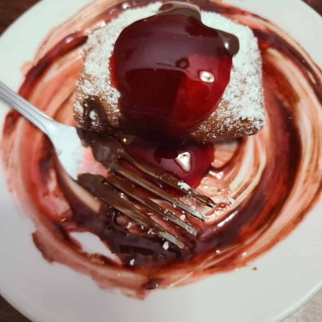 white plate drizzled and covered in chocolate and raspberry sauce with doughnut and a fork covered in chocolate