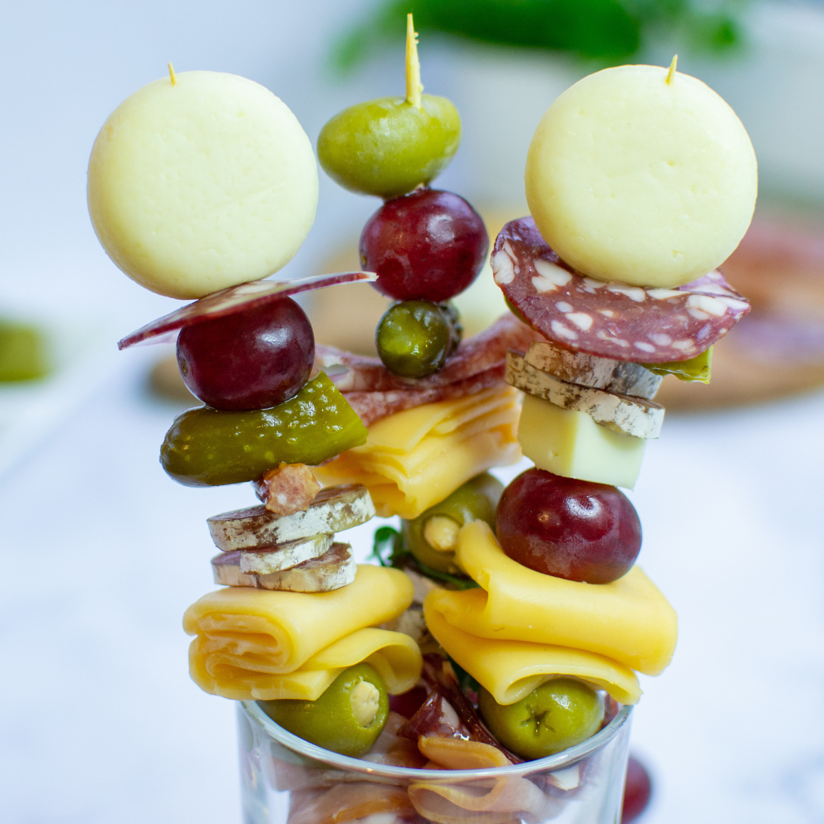 3 charcuterie skewers in glass cup standing up close up