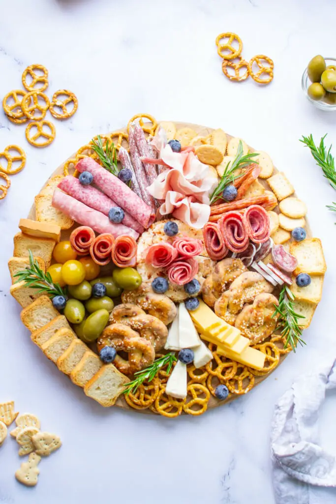 top view photo of pretzel charcuterie garnished with rosemary on a round wooden board