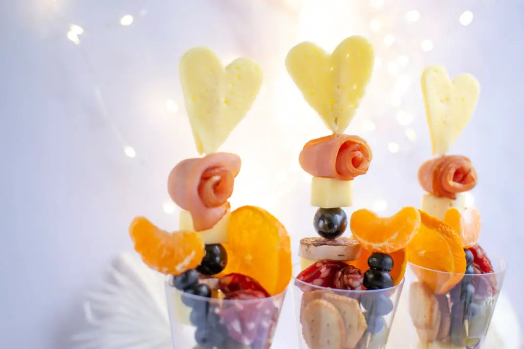3 charcuterie cups with sparkles in background and a heart shaped cheddar cheese on top