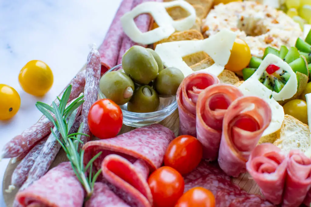 close-up view of salami, green olives, and grape tomatoes on the charcuterie board