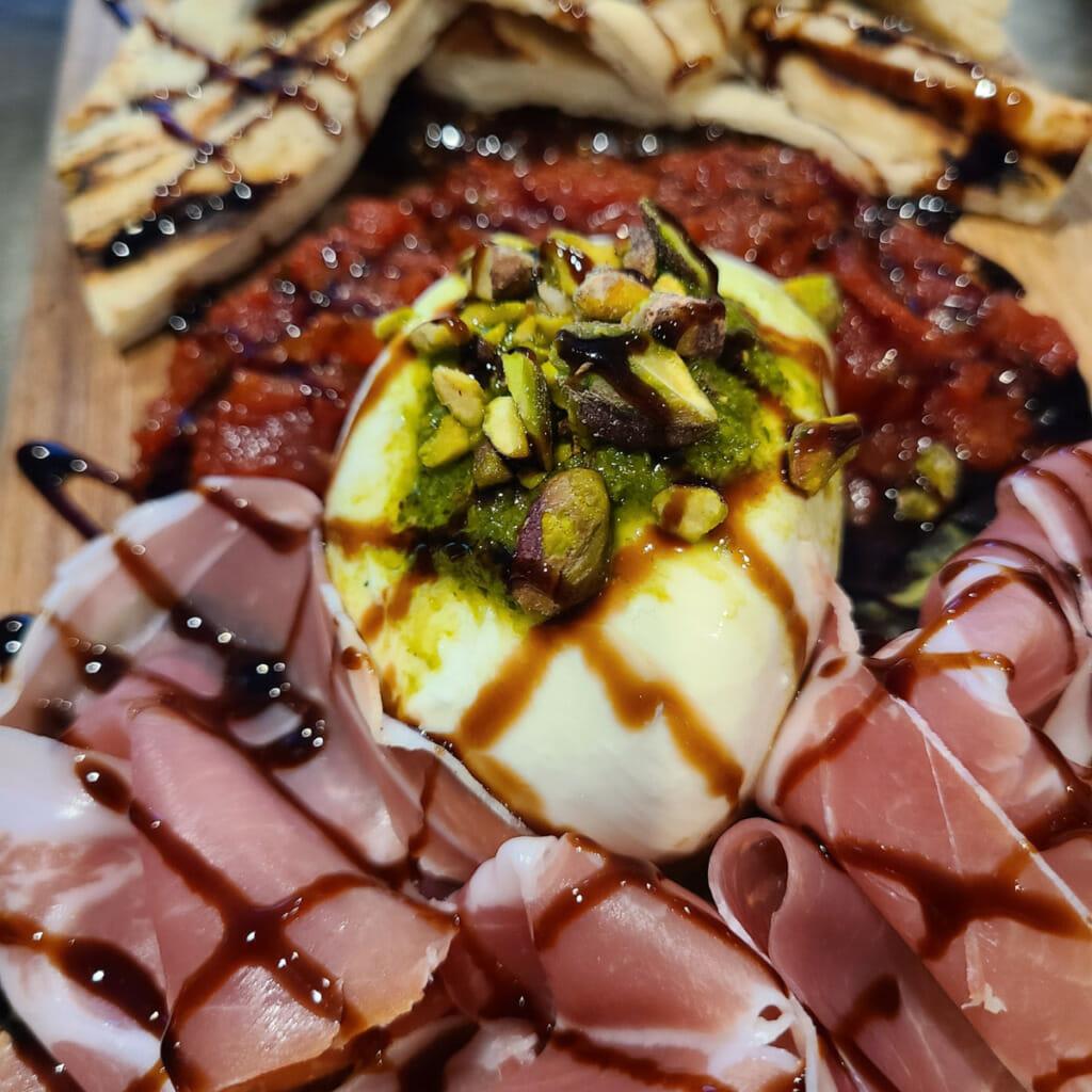 burrata cheese on cheeseboard topped with balsamic drizzle and pesto and nuts