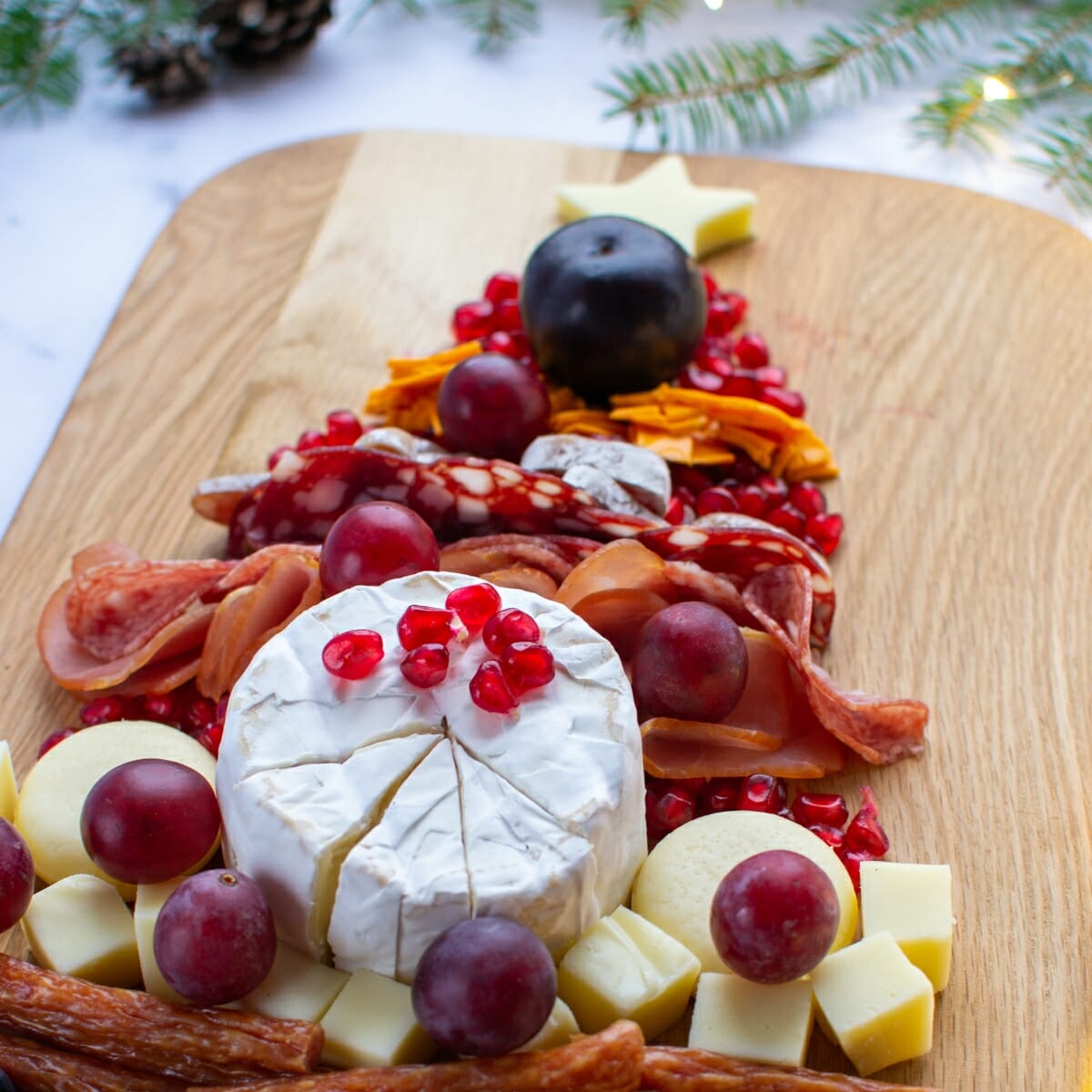 new year's eve charcuterie board - cheese pomegranate seeds and deli meat slices shaped like a christmas tree