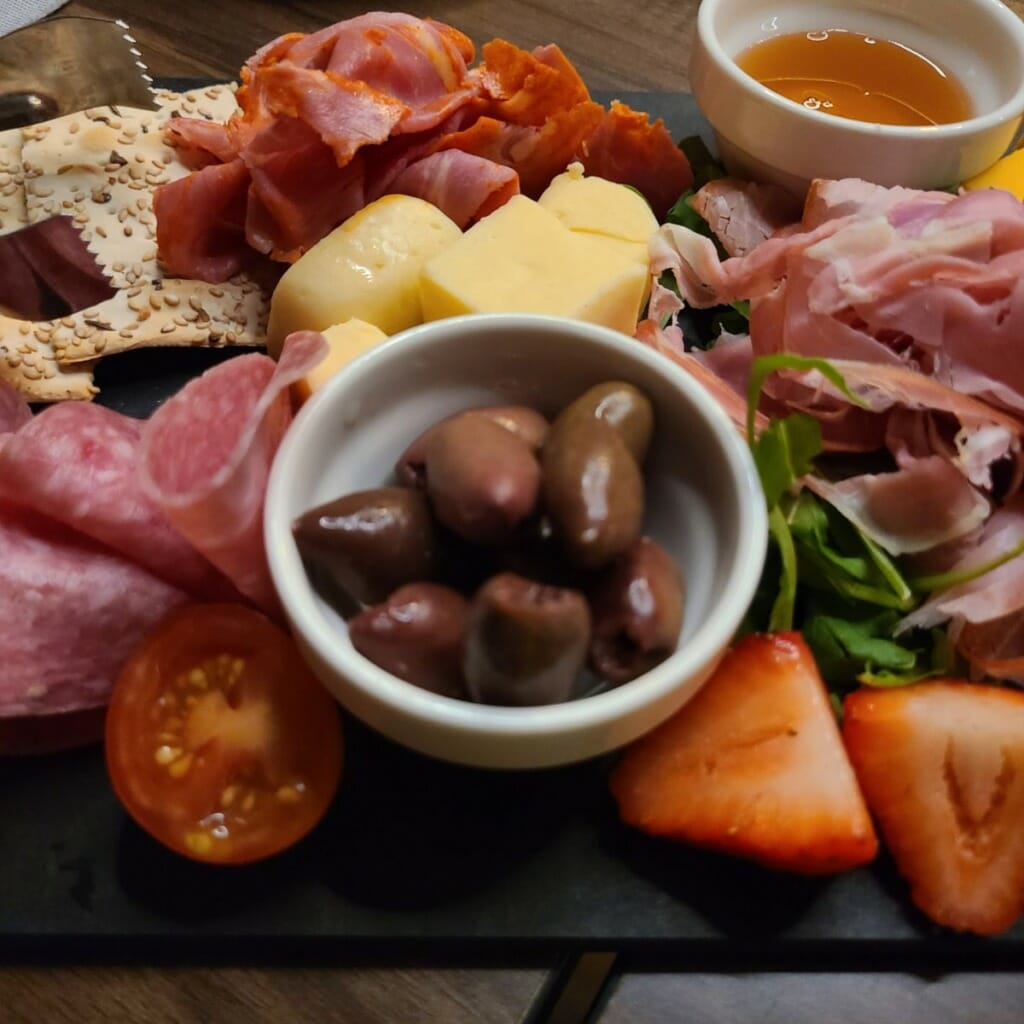 olives, honey, fruits on a charcuterie with meats and strawberries on background