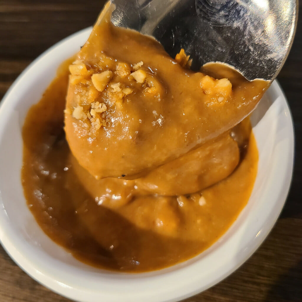 peanut hoisin dipping sauce close up on spoon with roasted peanuts on top