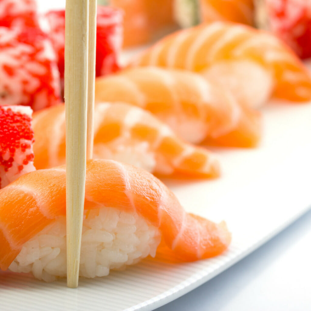 piece of oval shaped rice ball topped with raw salmon - chopsticks on it - nigiri