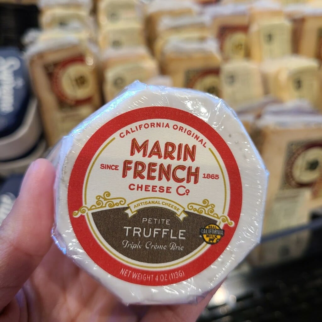 hand holding a triple creme brie at cheese counter