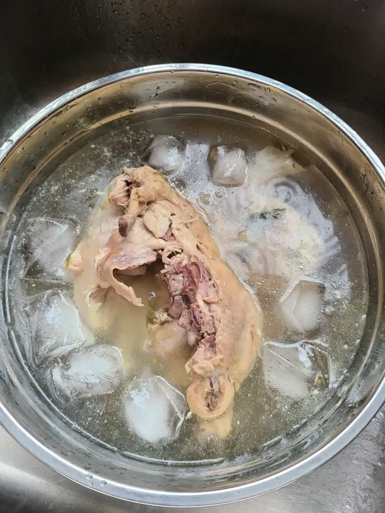 top view of cooked chicken in a pot with water and ice cubes