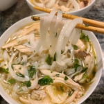 chopsticks pulling noodles out of a bowl of chicken pho