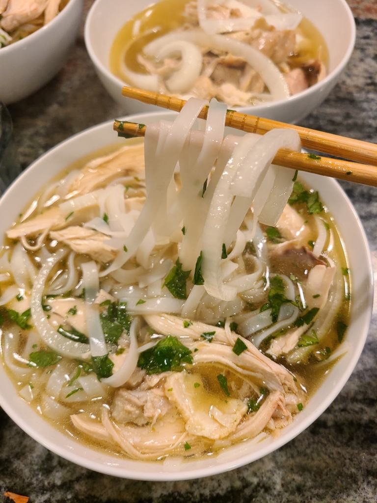 chopsticks pulling noodles out of a bowl of chicken pho