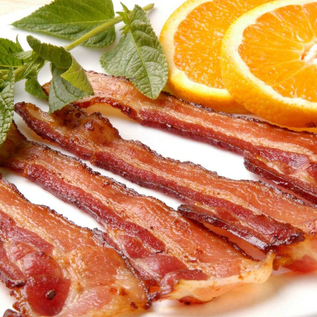 four strips of turkey bacon lying side by side next to layered orange slices and a branch of basil
