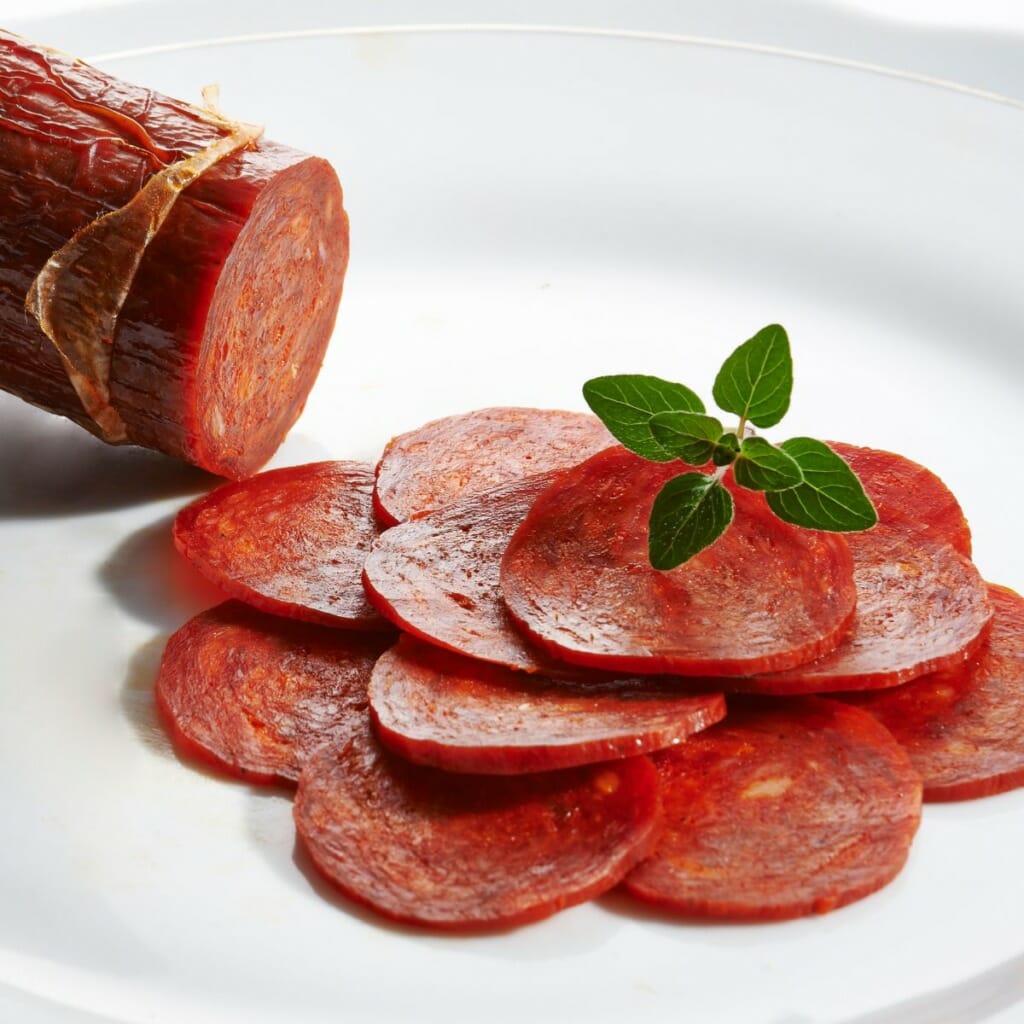 sliced pepperoni garnished with green herbs on a dish