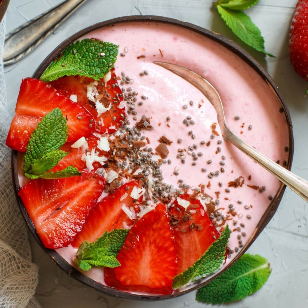 top view of strawberries, mint sprigs, and chia seeds atop a smoothie bowl without banana
