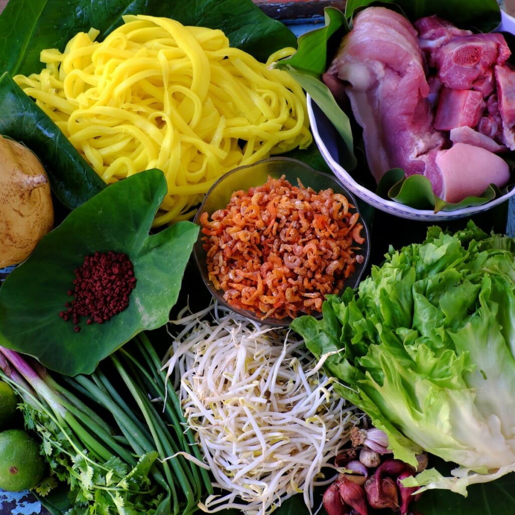 top view of the ingredients used to make mi quang - noodles, dried shrimp, lettuce, pork belly, beansprouts, pork neck bones