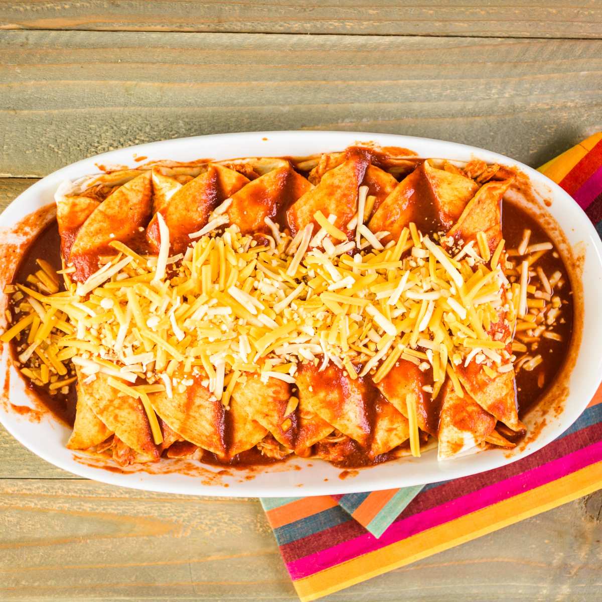 Enchiladas dipped in a sauce topped with cheese in a tray