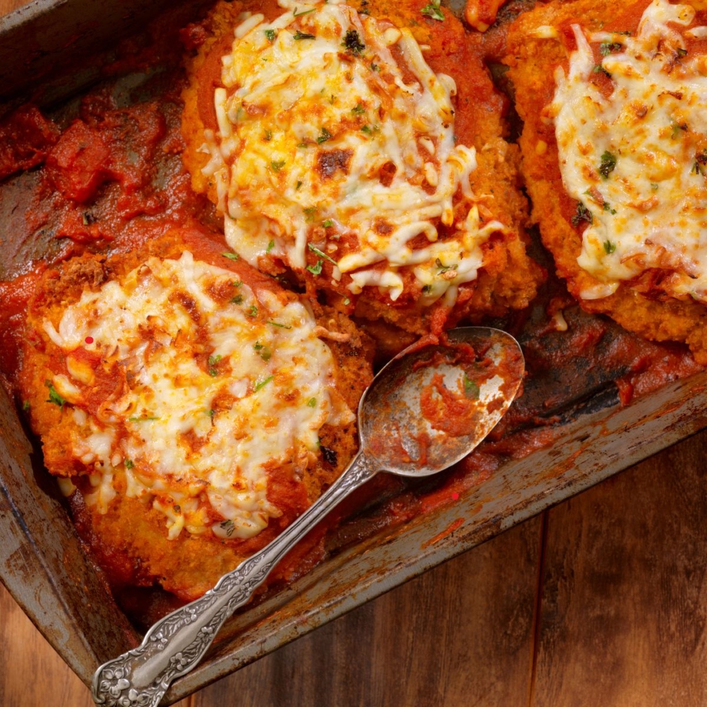 Chicken parmesan topped with cheese with spoon in a tray with a spoon on top of a table