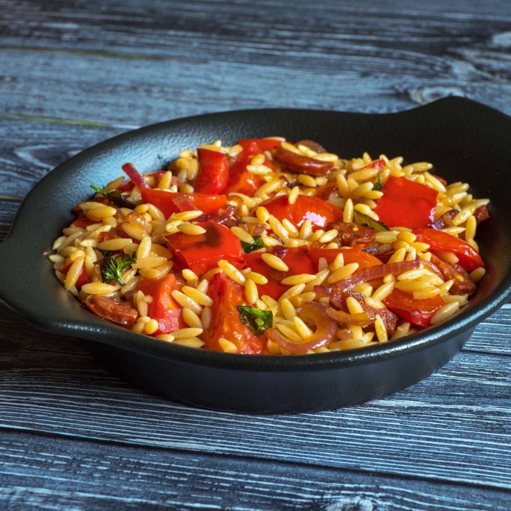 Orzo pasta topped with tomatoes in a plate on a table
