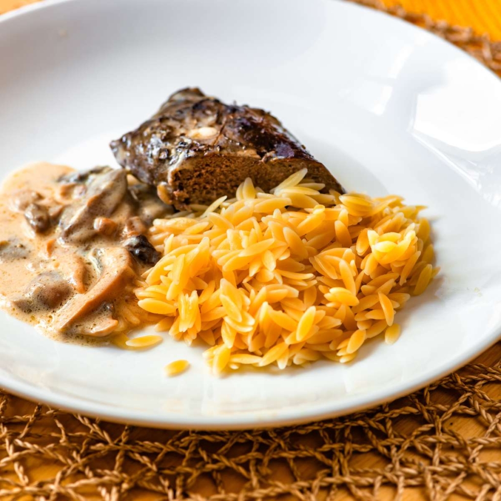 Orzo pasta with meat a sauce in a plate on a table
