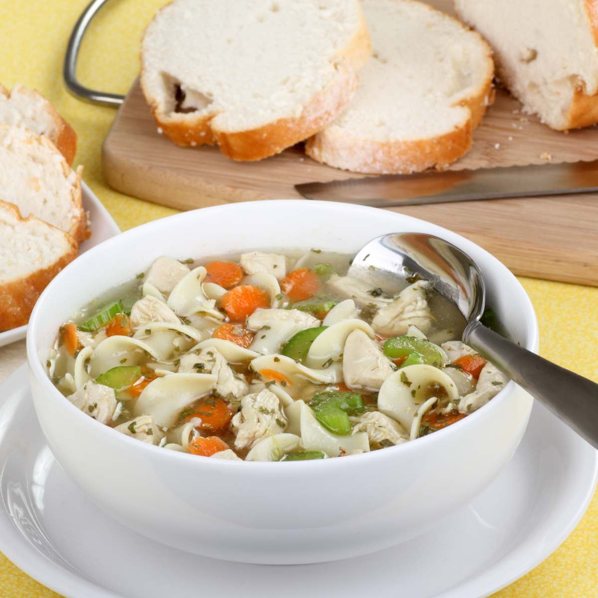 chicken noodle with capsicum,peas and carrot with spoon in a bowl and table
