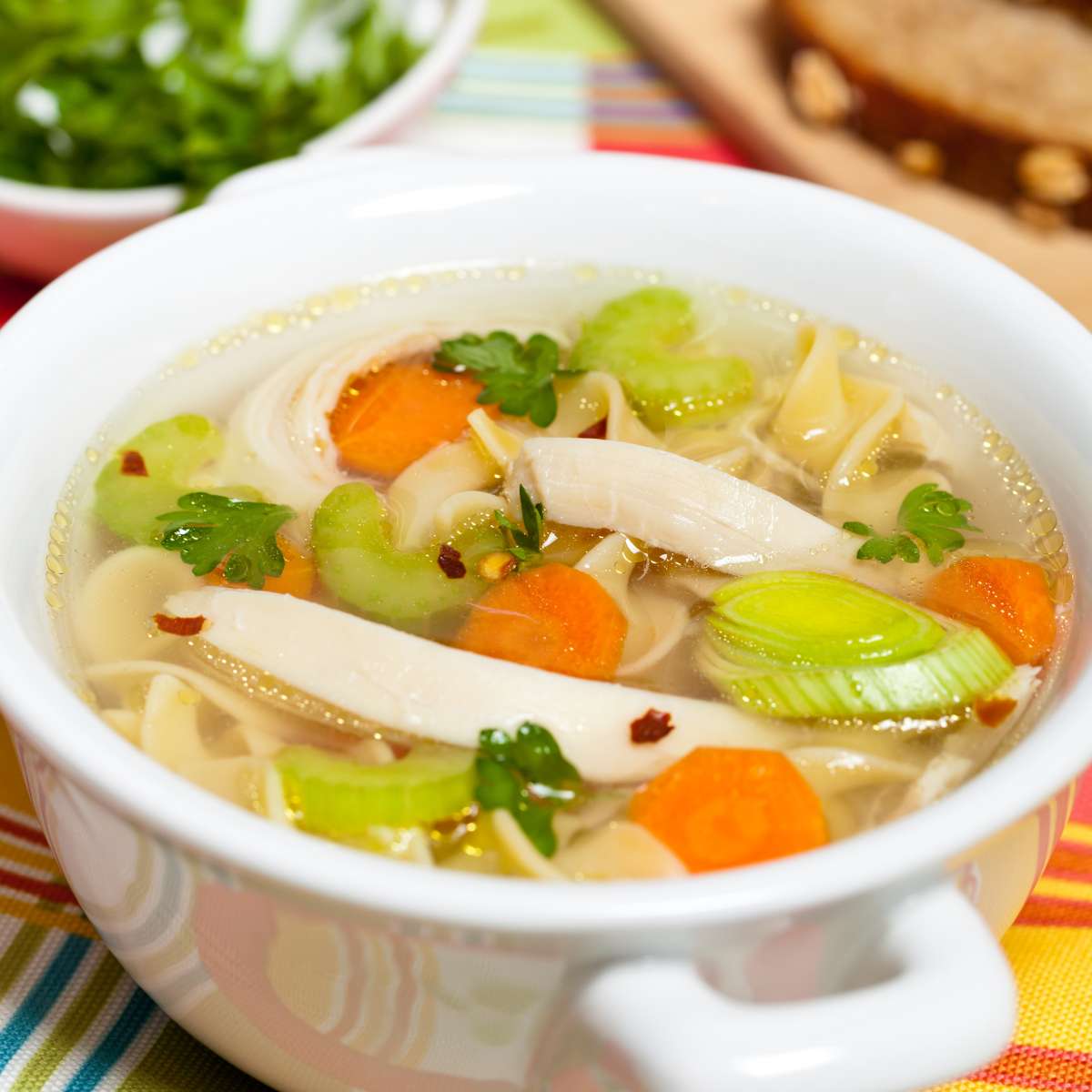 chicken noodle soup with green onion, peas and carrot in a pot on table
