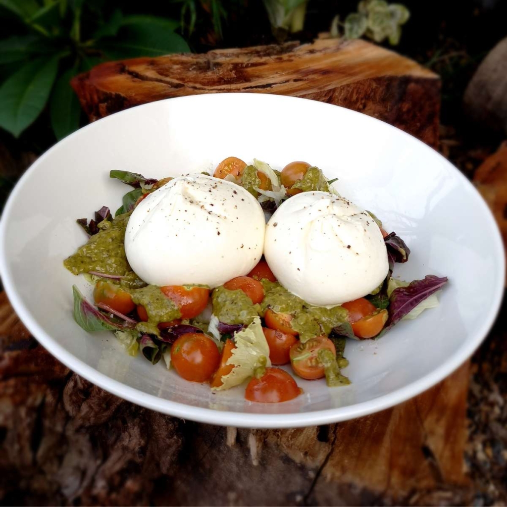 Two burrata with tomato and green sauce in a plate placed on a table 
