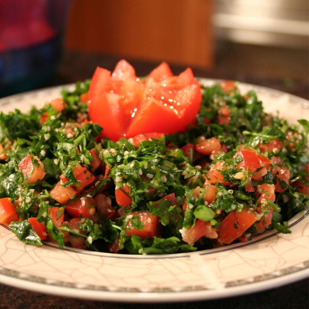 Tabouli salad topped with tomato in a plate placed on a table